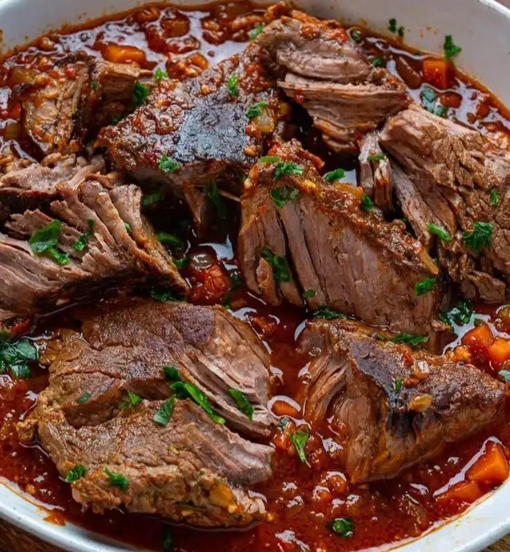 Ein dampfender, zarter Rinderschmortopf mit Tomatensauce und Karotten serviert in einer rustikalen Cocotte mit frischer Petersilie.